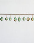 Decorative green eggs with gold accents hanging on a rod against a light blue background