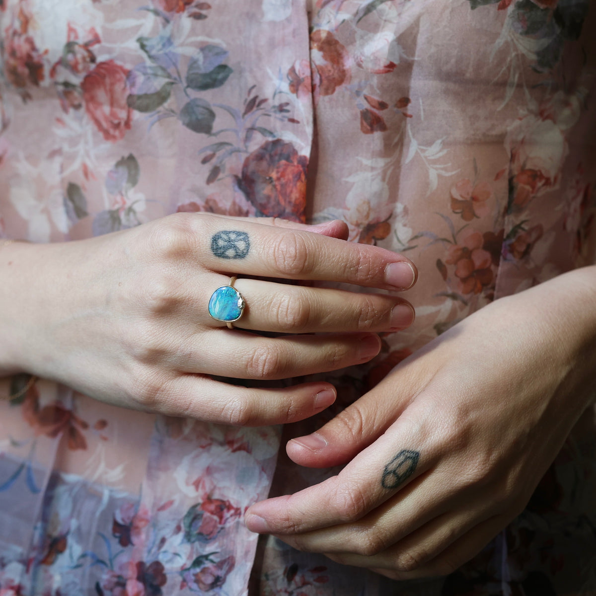 Woman wearing opal ring against a floral blouse. 