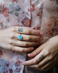 Woman wearing opal ring against a floral blouse. 
