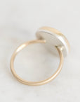 A minimalist gold ring with a flat, circular silver-toned top, photographed on a light gray marble surface.
