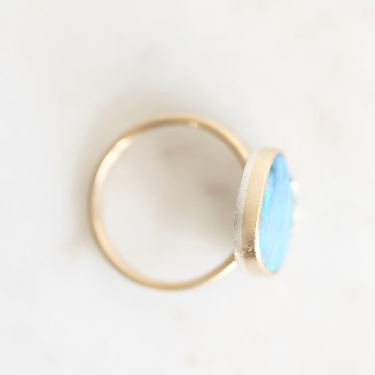 A gold ring with a flat, oval-shaped light blue stone, photographed on a clean white background.