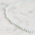 A delicate beaded necklace with white pearl-like beads and small turquoise blue accent beads, photographed on a light marble surface.