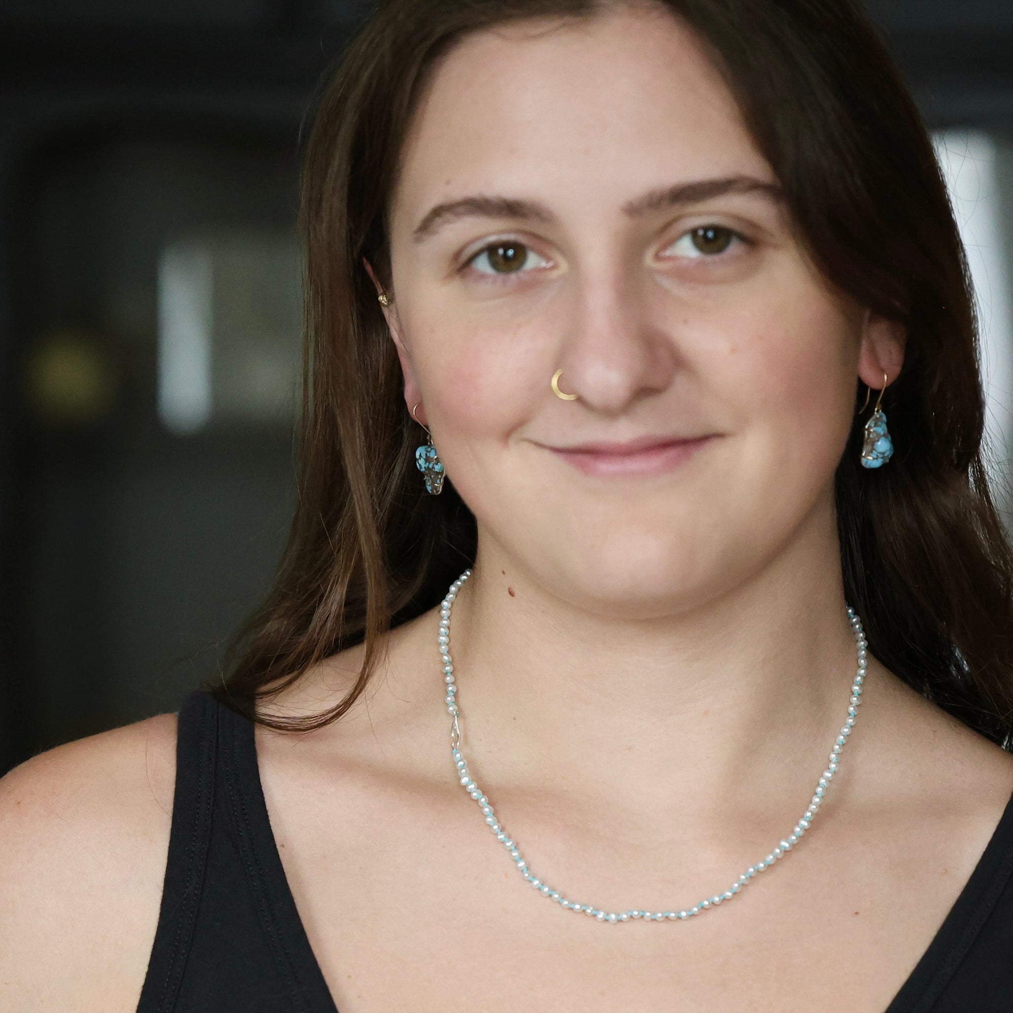 Small white pearl strand necklace on woman with brown hair and nose ring