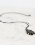 A black teardrop pendant necklace with a gold-toned spiked border, resting on a white marble surface.