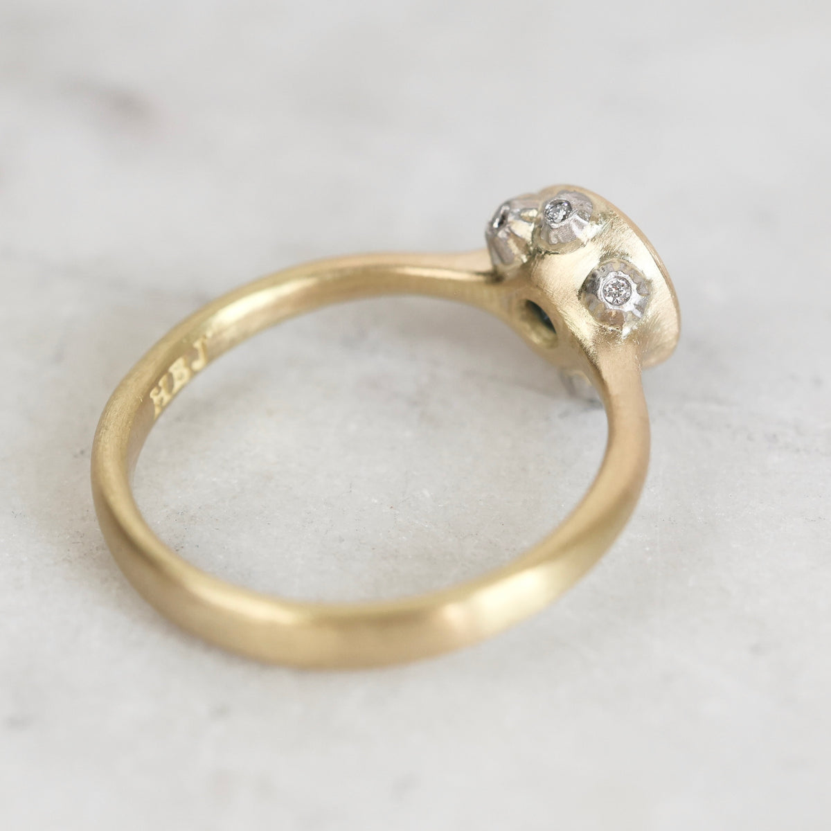 A close-up of a vintage yellow gold ring with a textured, organic-shaped setting holding three small clear stones, photographed on a light gray marble surface.