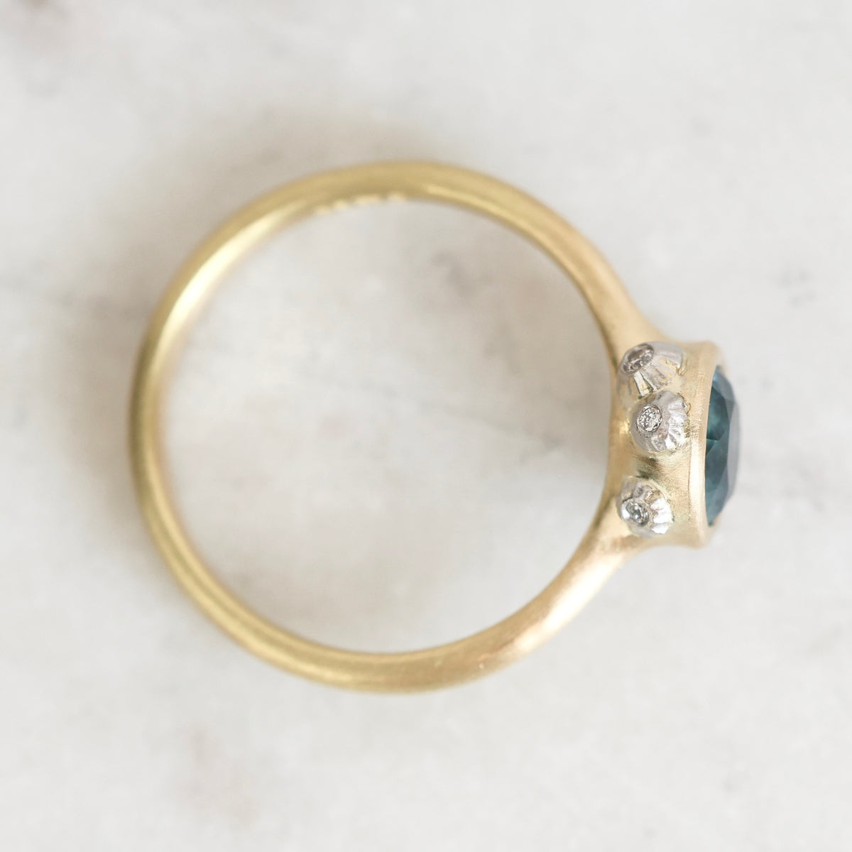 A gold ring with a dark blue oval center stone and three small clear accent stones, photographed from above on a light marble-like surface.