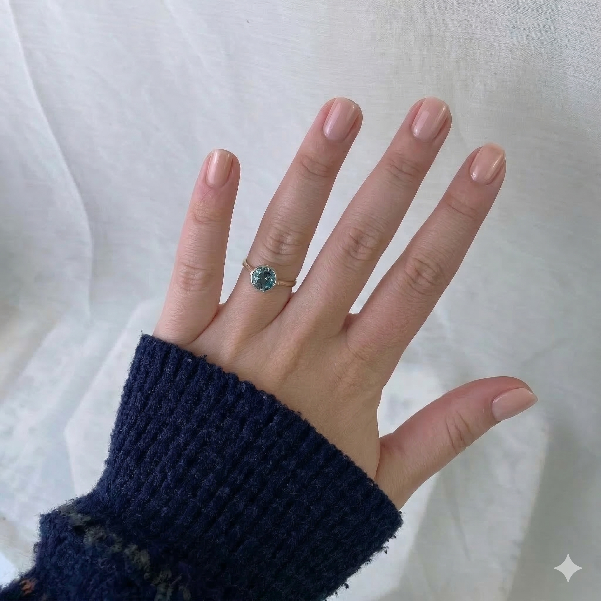 Hand wearing gold ring with blue gemstone on a white fabric background 