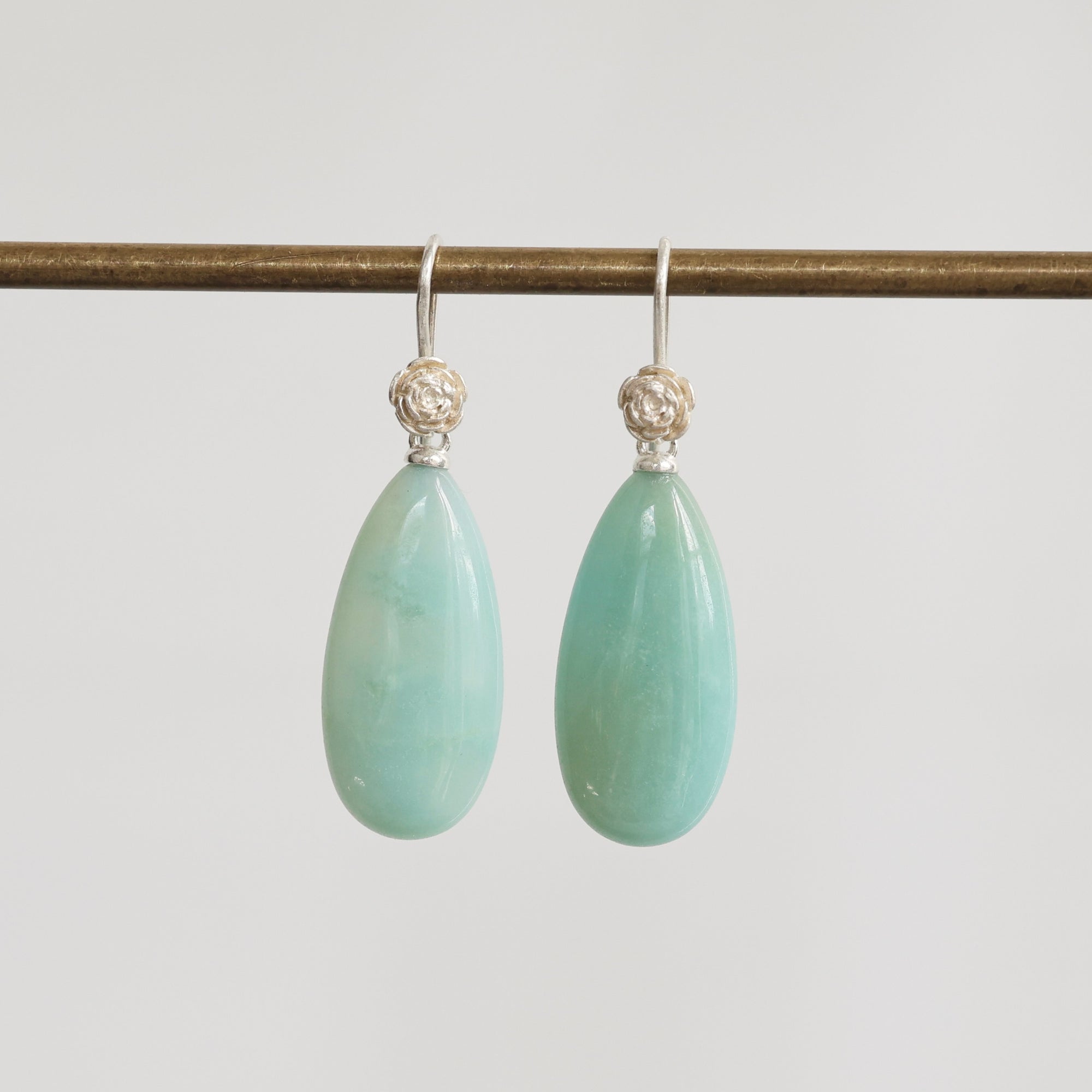 Teardrop-shaped green earrings with silver hooks on a light gray background