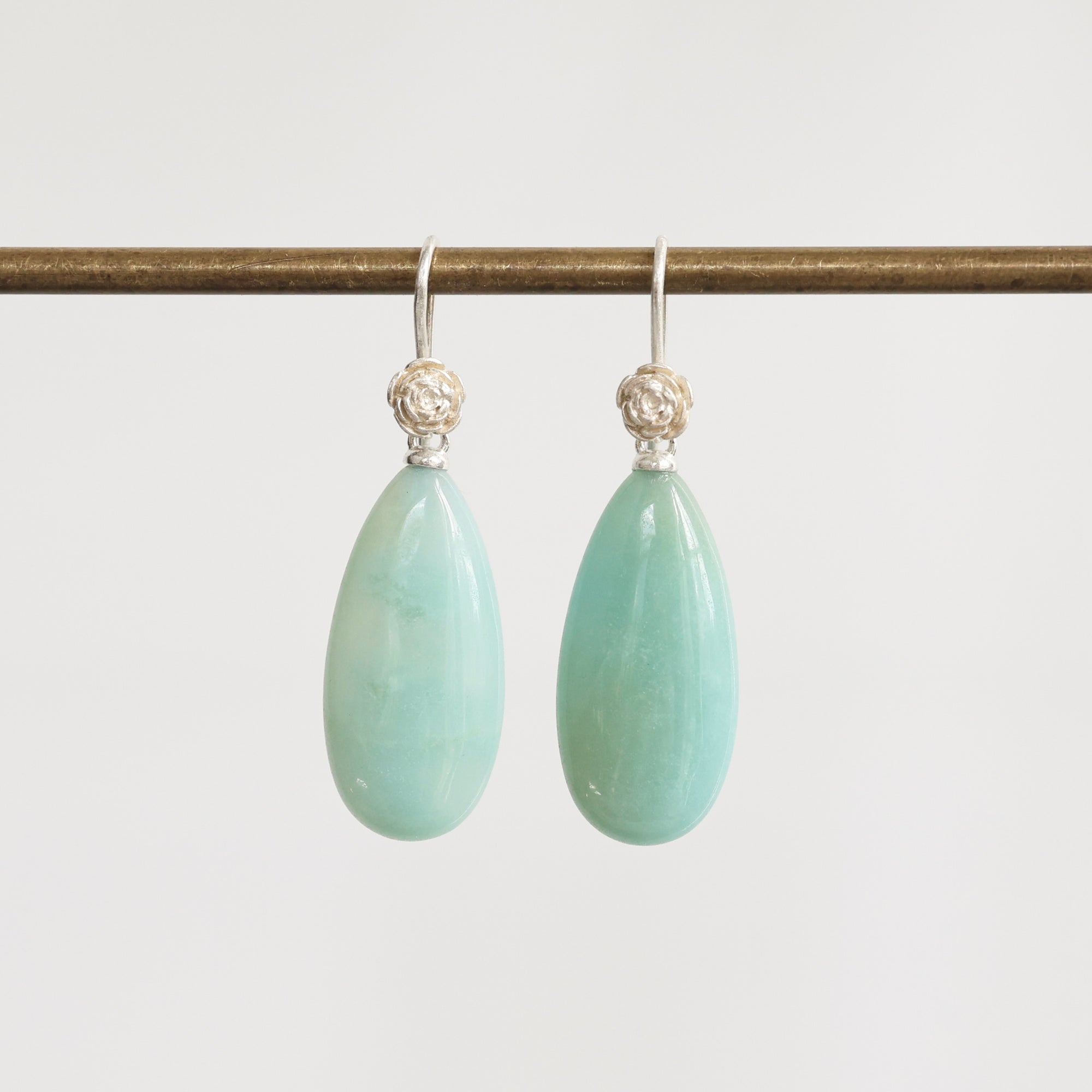 Pair of light green teardrop earrings with silver hooks on a white background