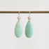 Pair of light green teardrop earrings with silver hooks on a white background