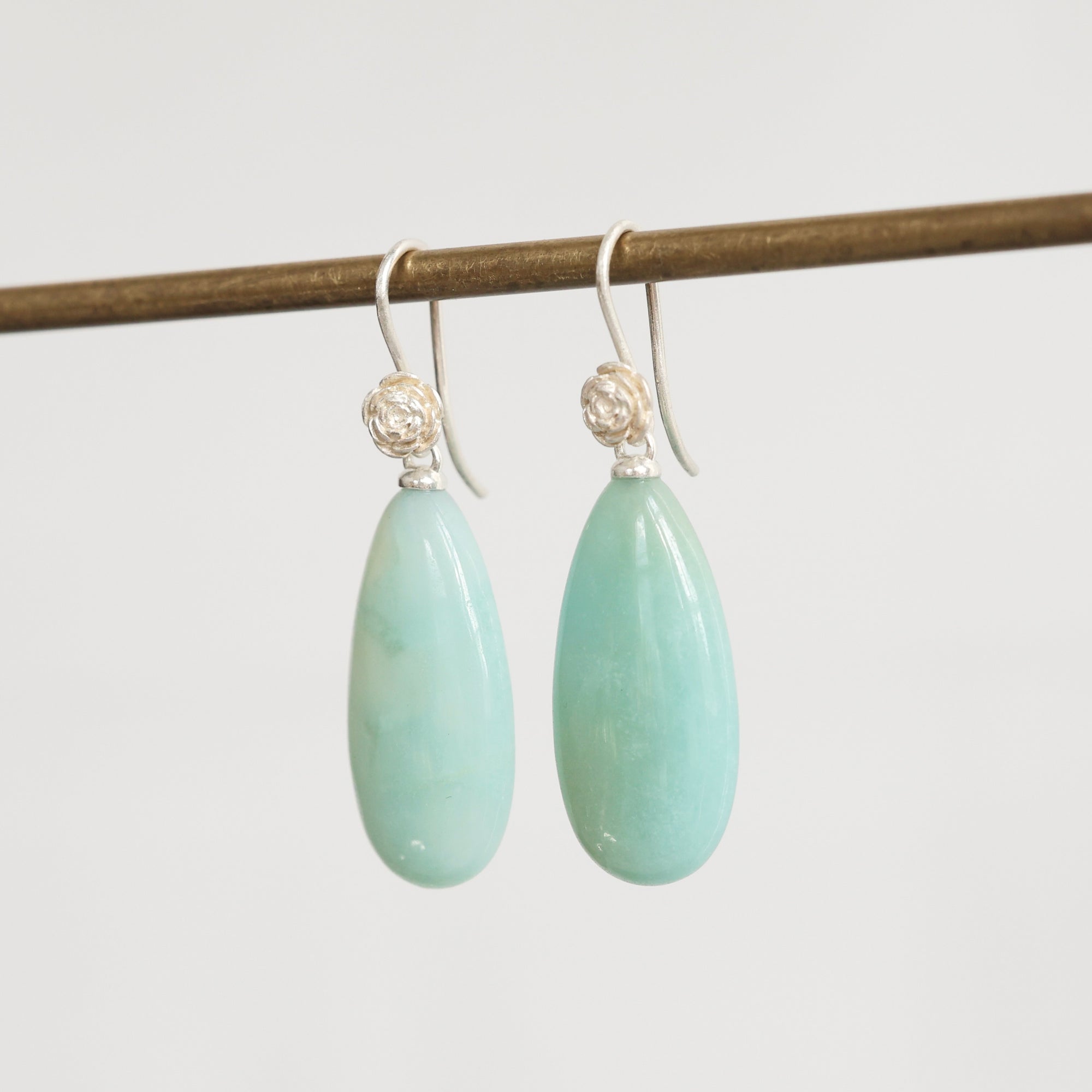 Teardrop-shaped green earrings with silver hooks on a white background