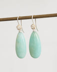 Teardrop-shaped green earrings with silver hooks on a white background