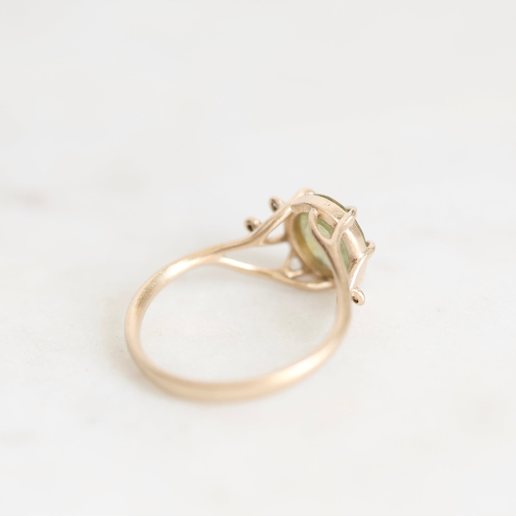 A gold ring with a small light green gemstone in a prong setting, photographed on a clean white background.