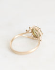 A gold ring with a small light green gemstone in a prong setting, photographed on a clean white background.