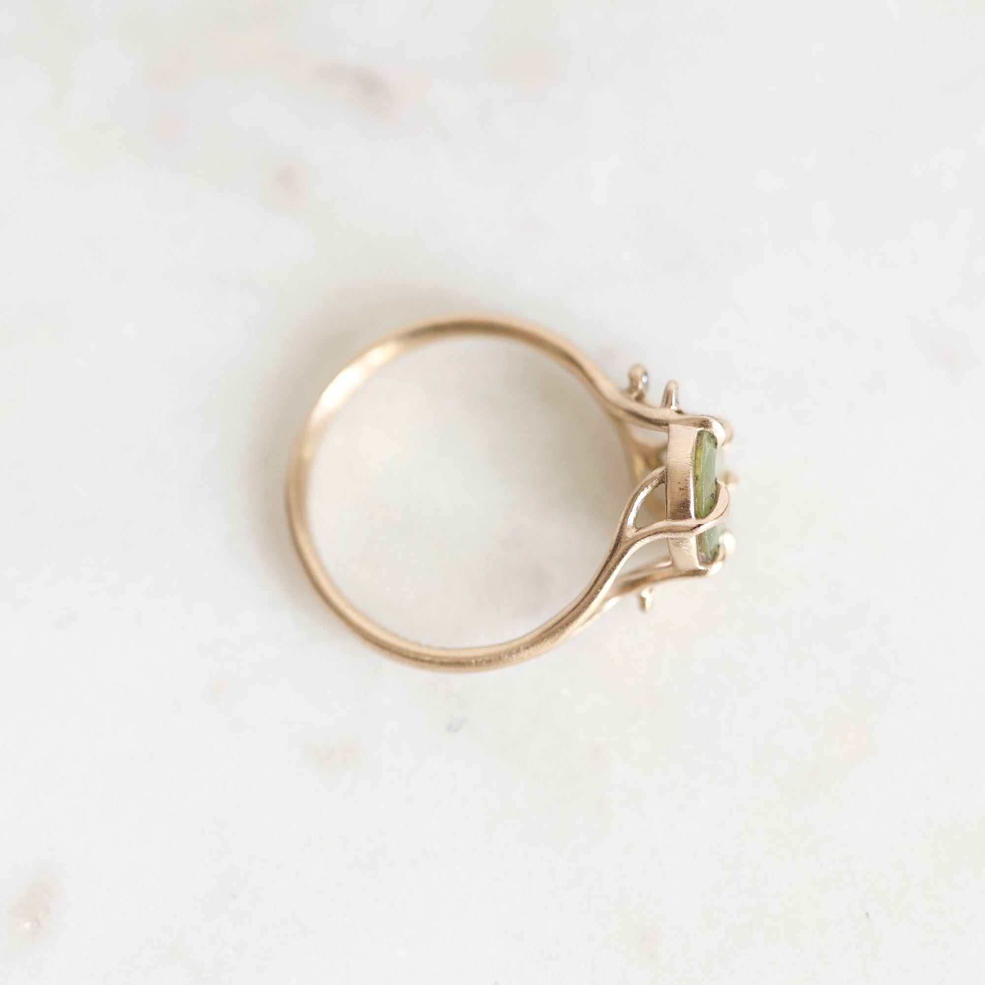 A gold ring with a small green gemstone, photographed on a light marble surface.