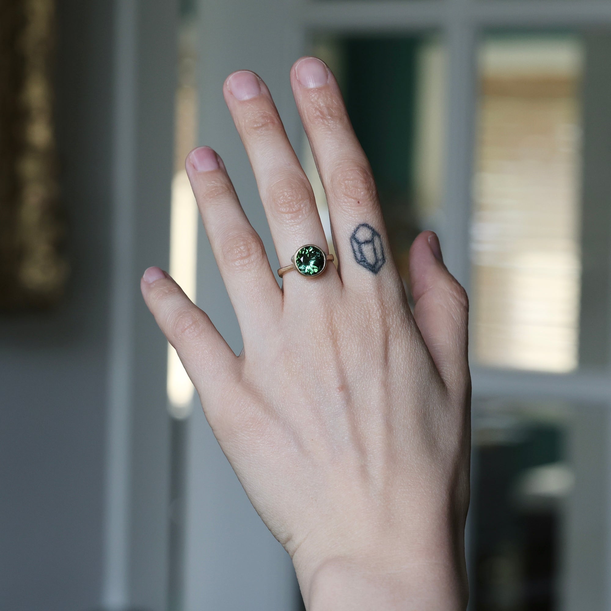 Hand with a green gemstone ring and tattoo, blurred background