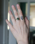 Hand with a green gemstone ring and tattoo, blurred background