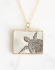 A rectangular pendant necklace featuring a mother-of-pearl inlay with a black engraved sea turtle design, suspended from a delicate gold chain on a light marble background.