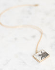 A gold chain necklace with a square pendant featuring a silver-toned sea turtle illustration, displayed on a white marble surface.
