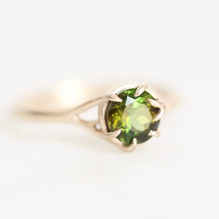 A silver ring with a round-cut green gemstone in a prong setting, photographed on a clean white background.