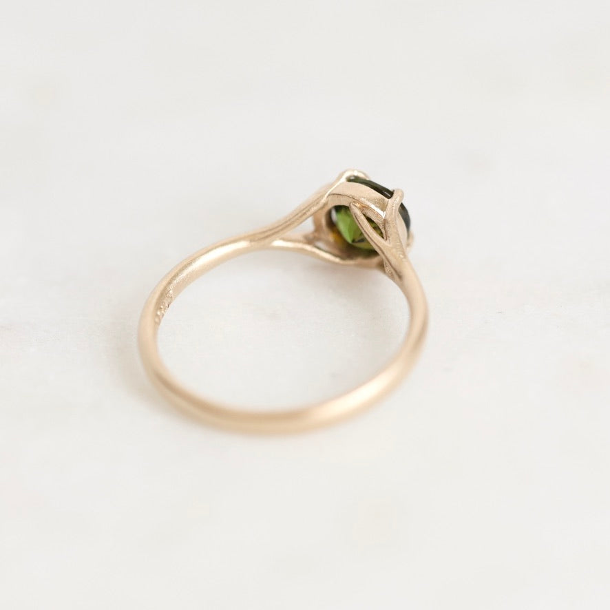 A gold ring with a small green gemstone in a prong setting, photographed on a plain light background.