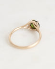 A gold ring with a small green gemstone in a prong setting, photographed on a plain light background.