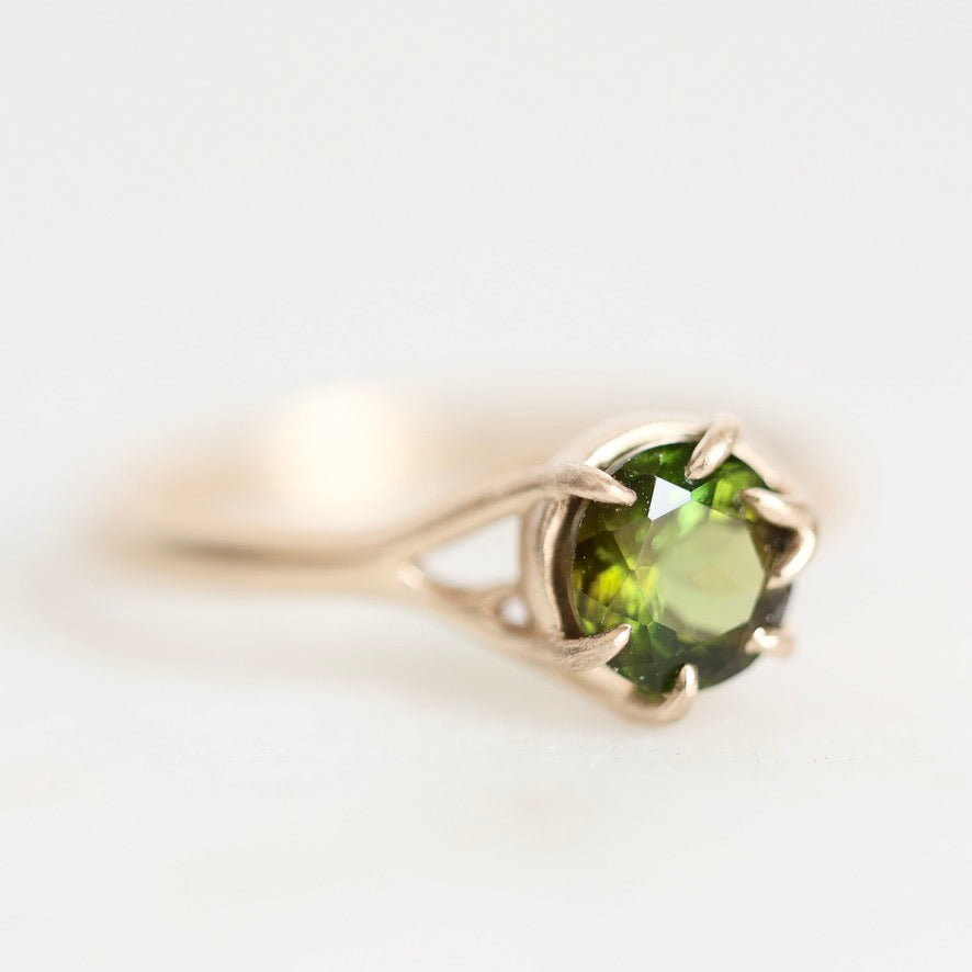 A gold ring featuring a round green gemstone in a prong setting, photographed on a clean white background.