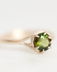 A gold ring featuring a round green gemstone in a prong setting, photographed on a clean white background.