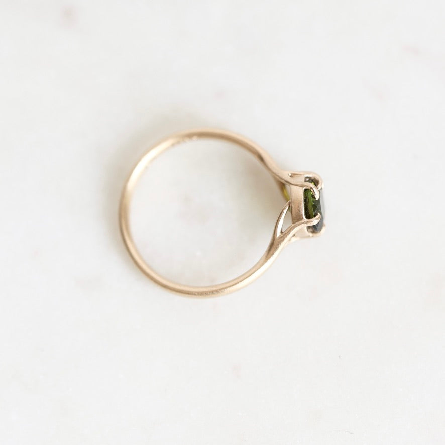 A gold ring with a small green gemstone, photographed from an overhead angle on a light, off-white marble surface.