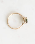 A gold ring with a small green gemstone, photographed from an overhead angle on a light, off-white marble surface.