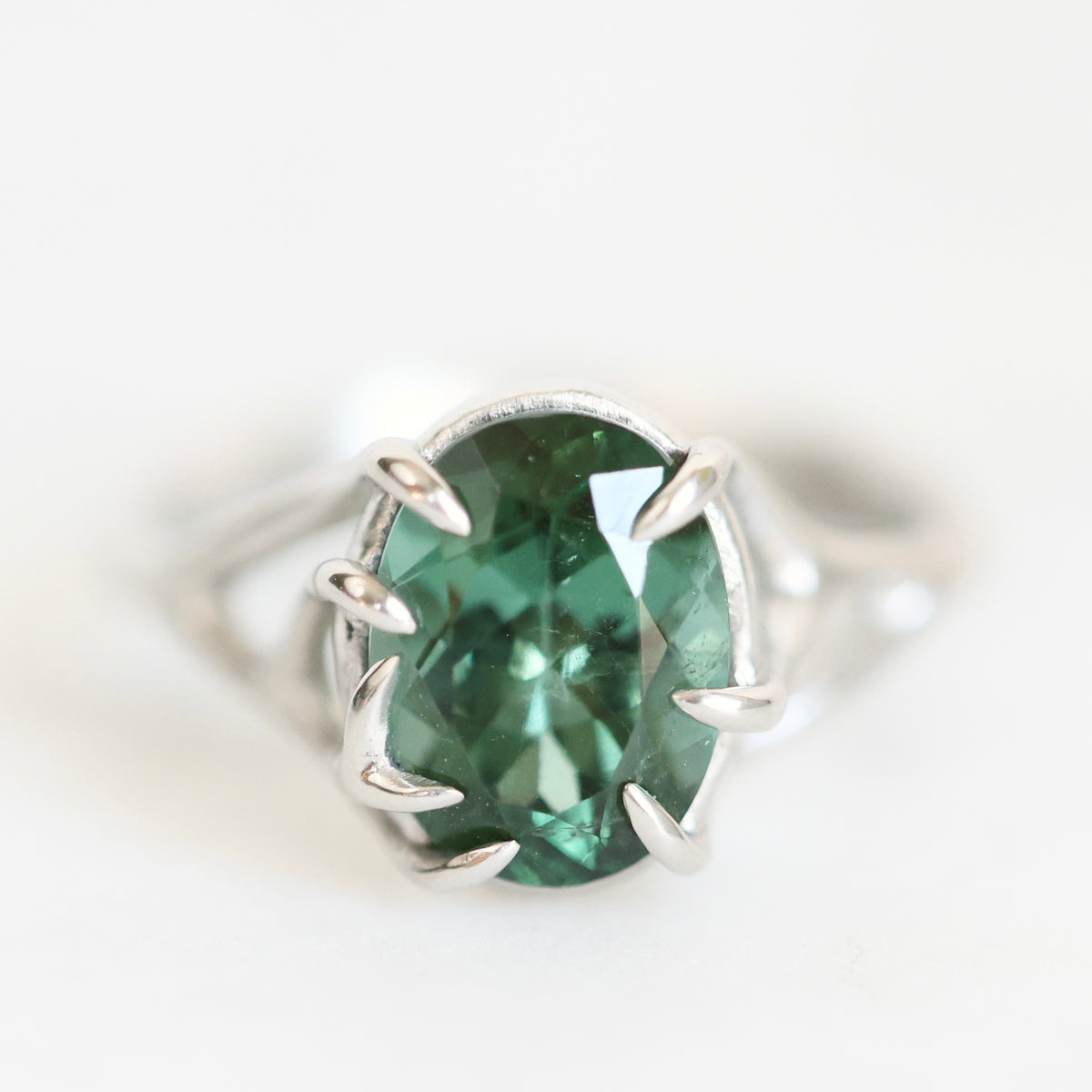A silver ring featuring a large, oval-cut green gemstone in a prong setting, photographed against a clean white background.