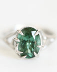 A silver ring featuring a large, oval-cut green gemstone in a prong setting, photographed against a clean white background.