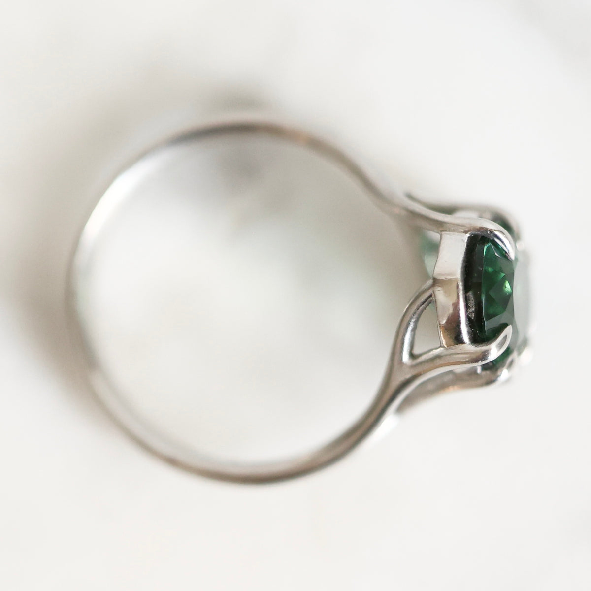 A silver ring with a marquise-cut green gemstone, shown in a close-up side view on a soft white background.