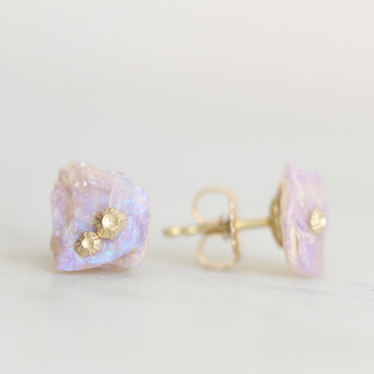 Raw opal studs with gold barnacle details against a white background. 