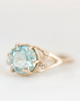 A gold ring featuring a large oval light blue gemstone in a prong setting, with small round accent stones on the band, photographed against a soft white background.