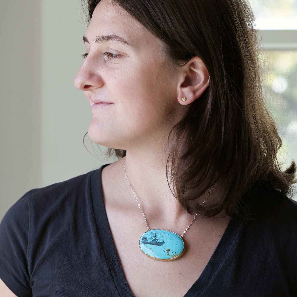 Woman wearing large turquoise pendant necklace looking out the window against a blurred indoor background.