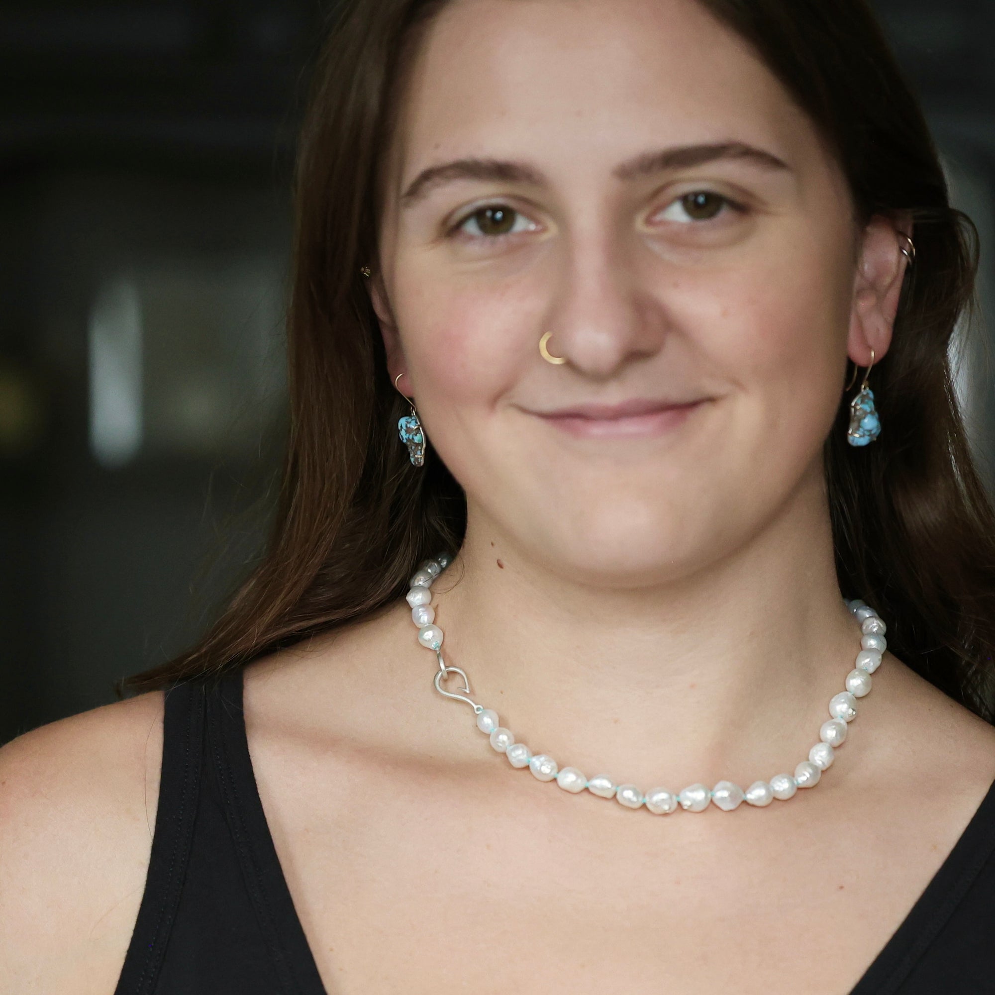 A woman with brown hair wearing a white baroque pearl necklace with a silver clasp and matching blue teardrop earrings, shown in a close-up portrait.