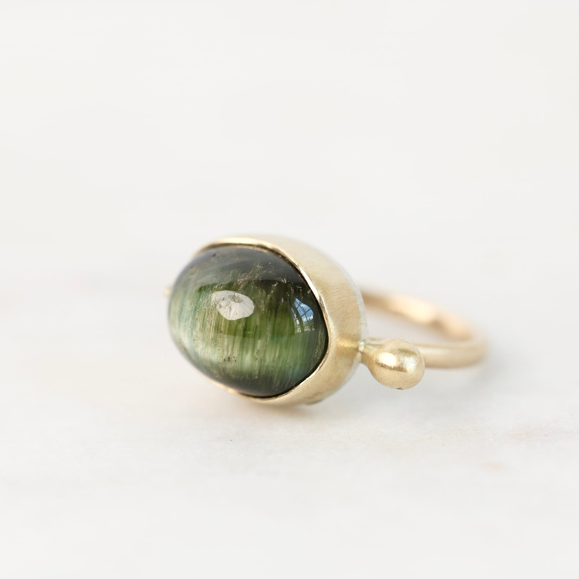 A gold ring featuring a large oval green cat's eye stone, photographed on a clean white background.