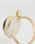 A close-up of a gold ring with a textured circular gold and silver-toned face, featuring a small gold protruding bead on top and a dark inlay on the side, set against a plain white background.