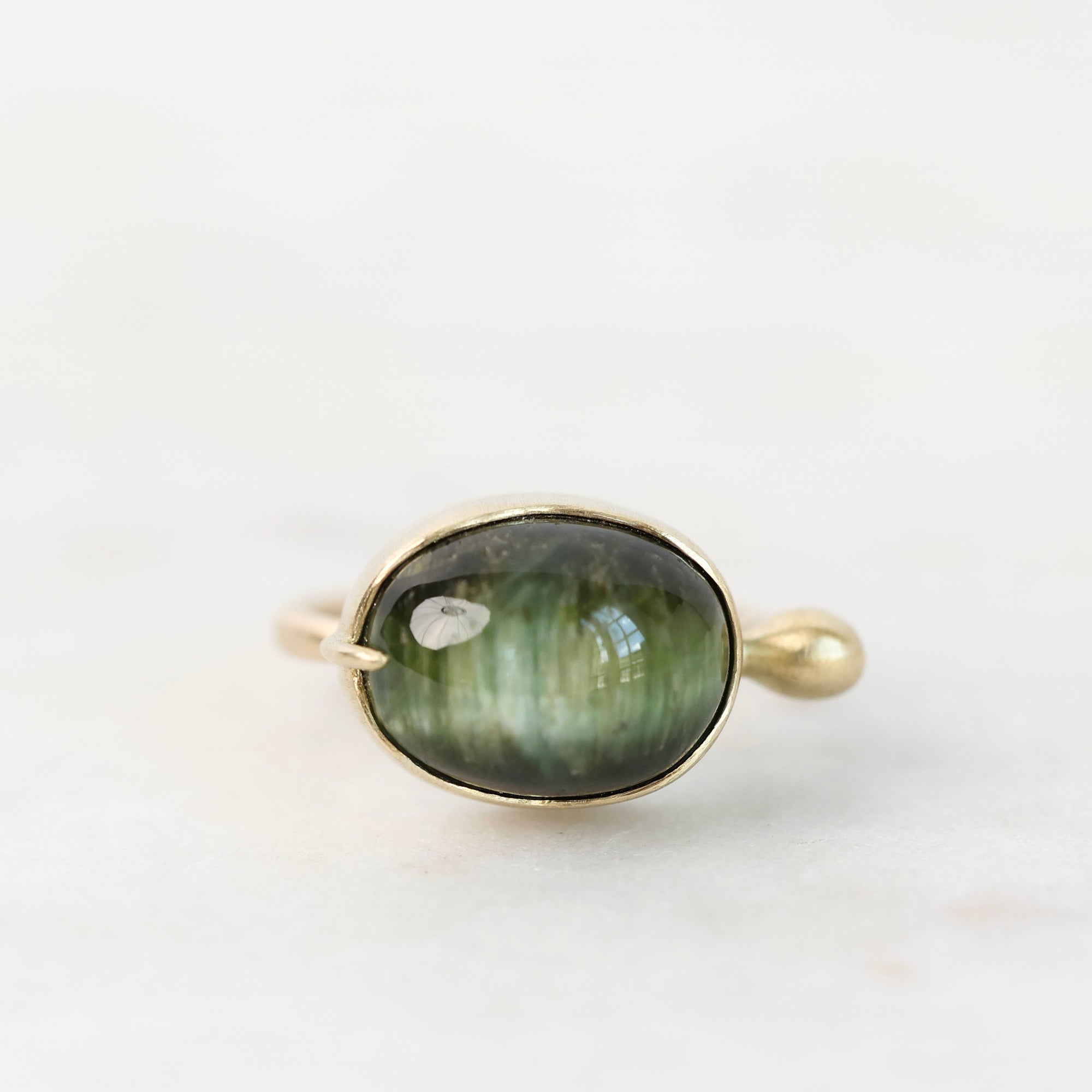 A gold ring featuring an oval green labradorite stone with natural iridescent shimmer, set against a clean white background.