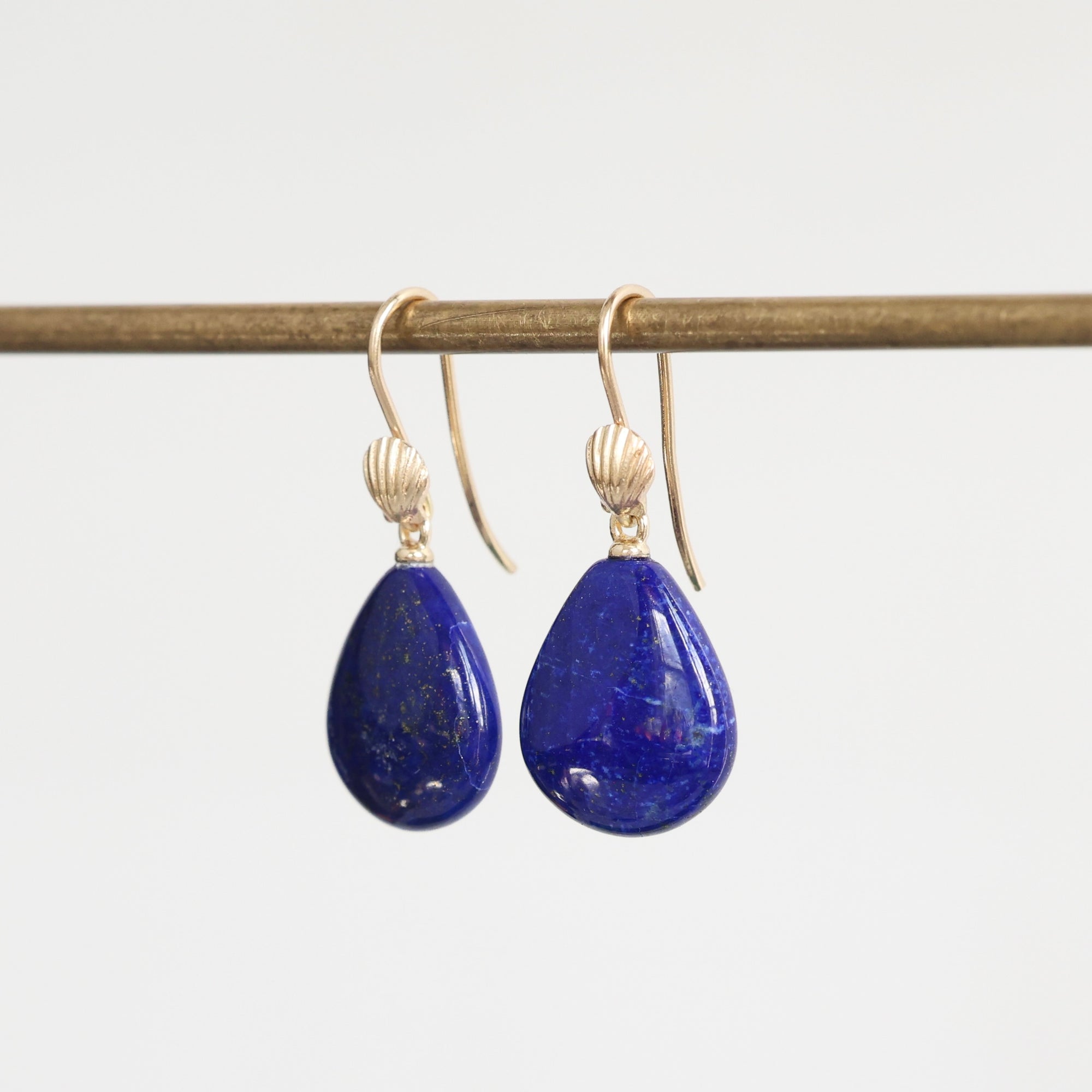 Bright blue lapis earrings hanging from bar with gold ear wires that have shell details 