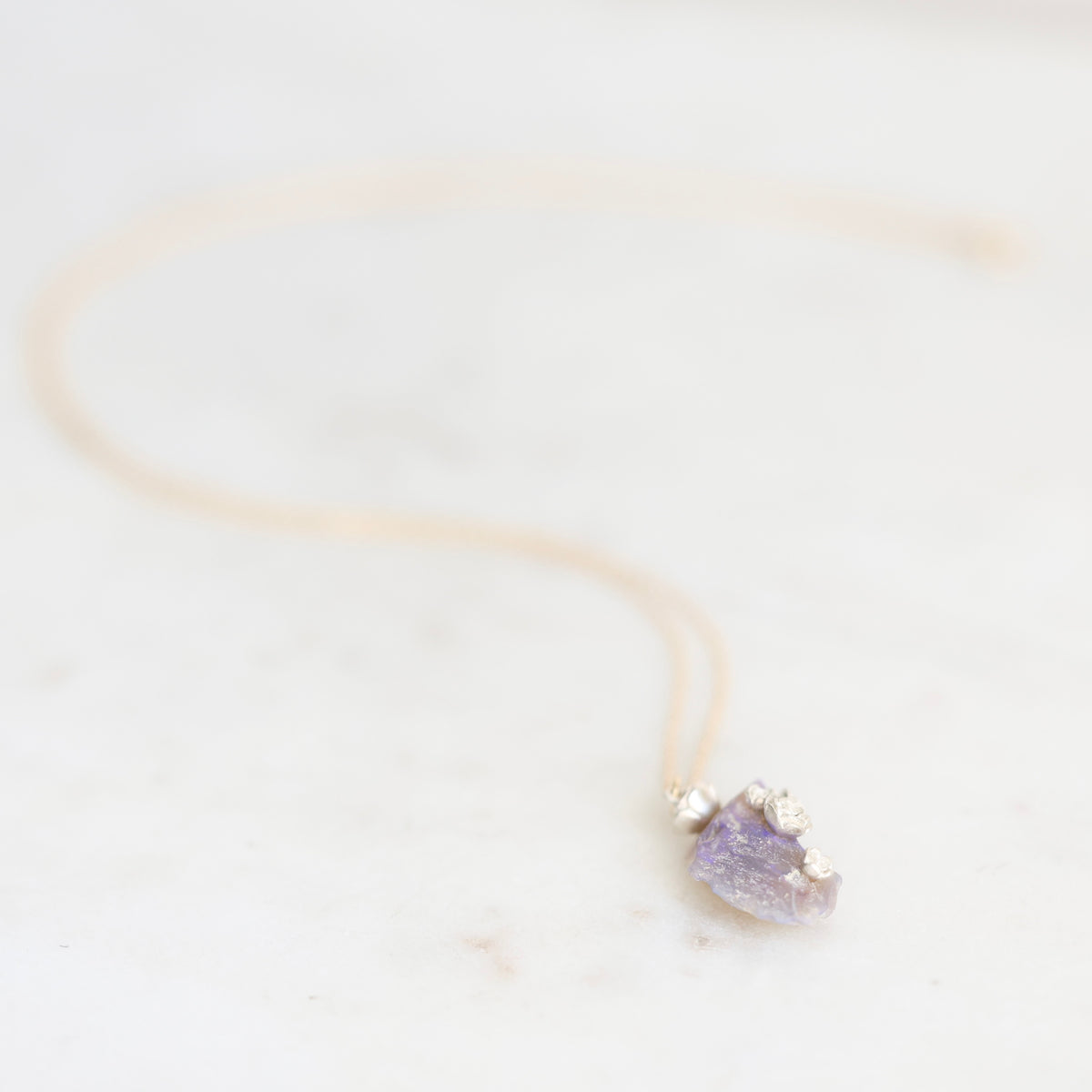 Bright purple fossilized opal with silver rose details suspended from a gold chain against a marble background. 