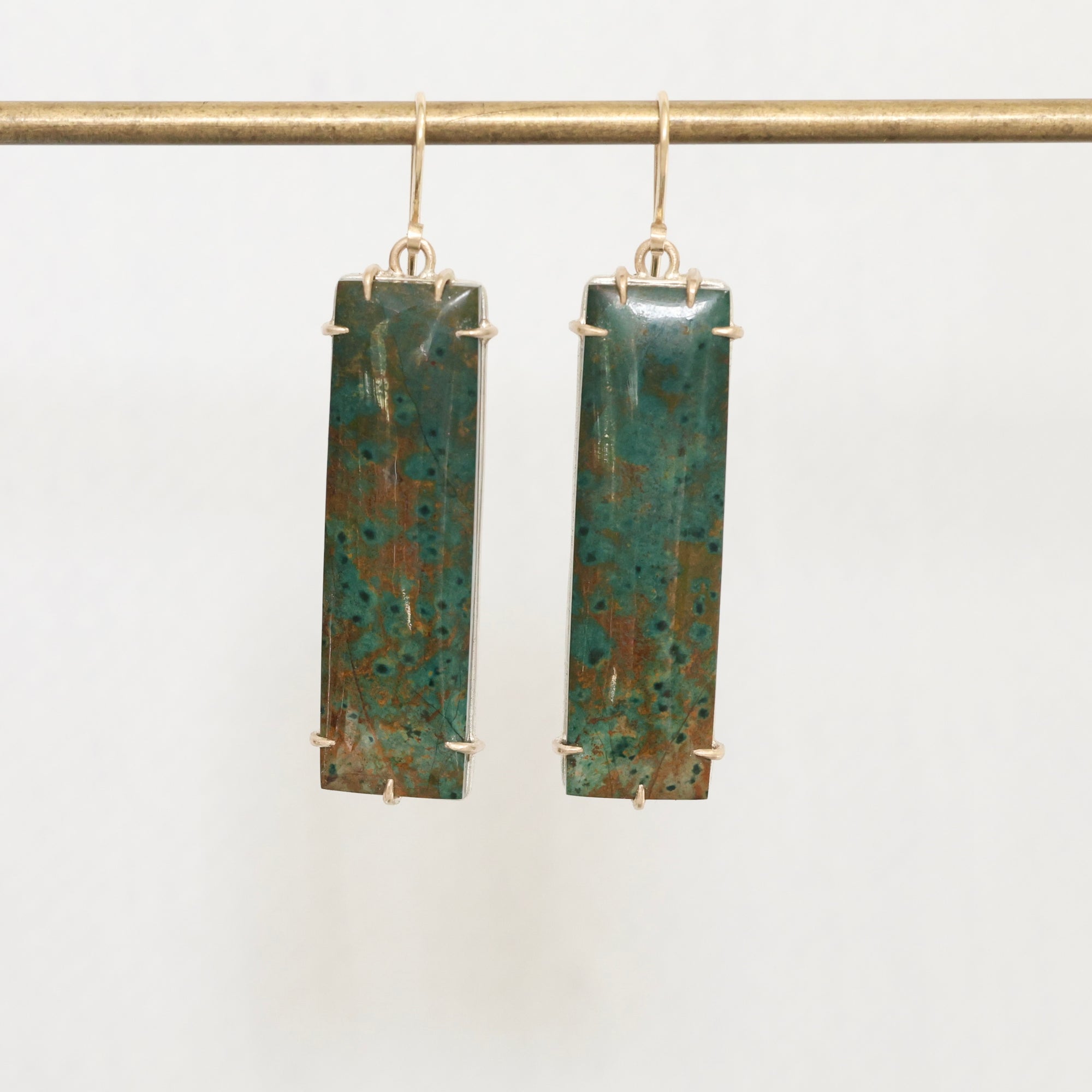 Long jasper drop earrings with gold prongs hanging on a gold bar 