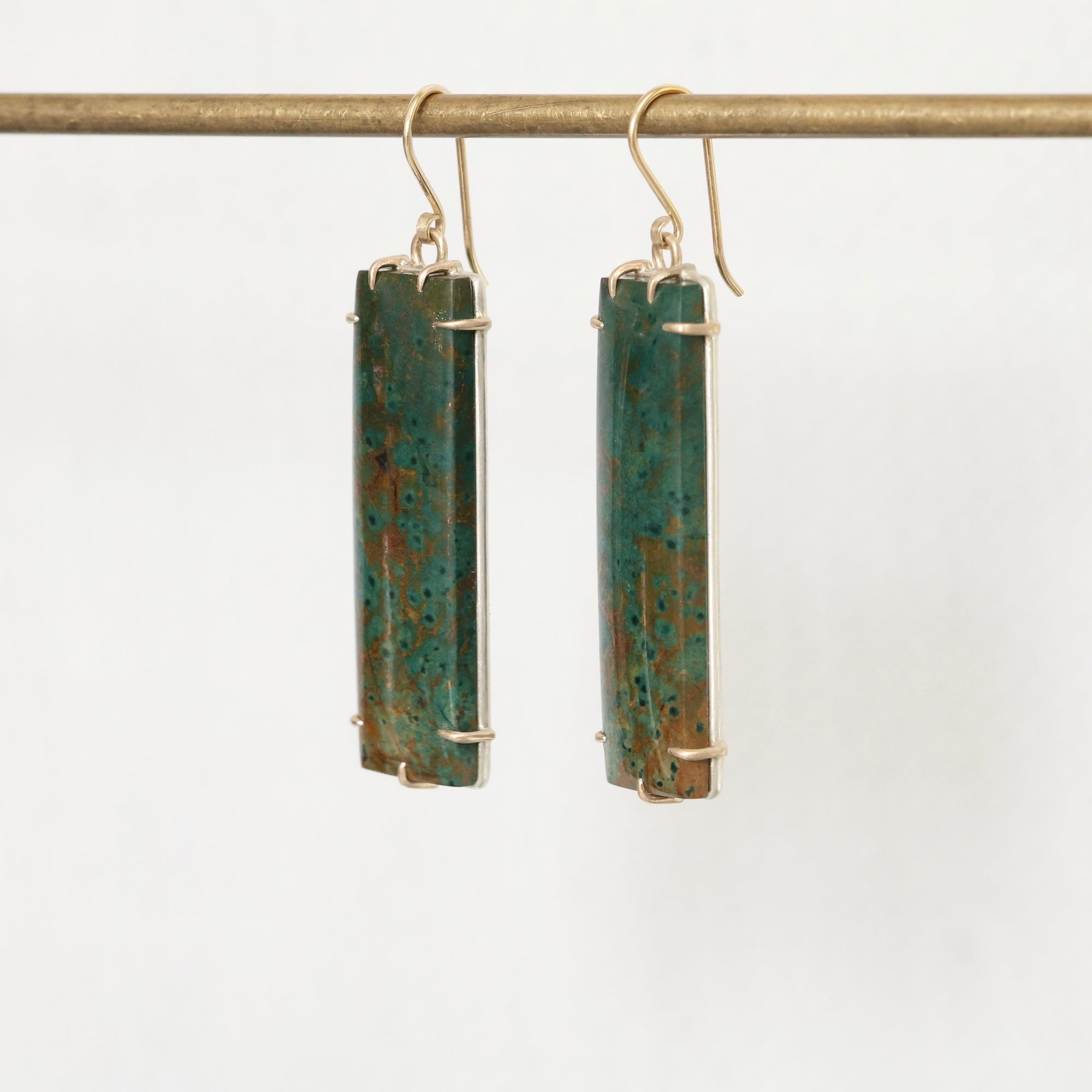 Pair of earrings with rectangular green stones on a white background