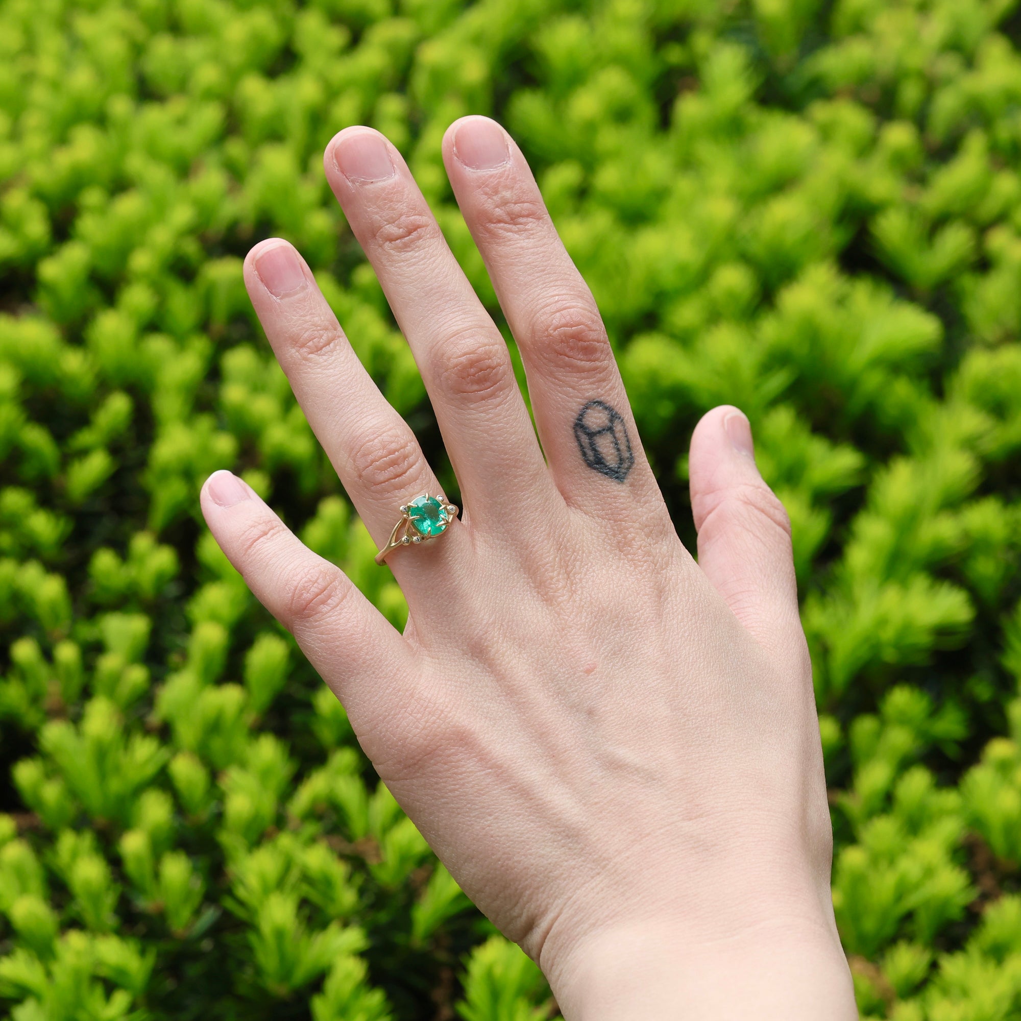 Bright green stone ring with diamonds and branchy prongs on hand