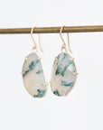 A pair of gold drop earrings with irregular white and green marbled stone pendants, hanging from a gold-colored horizontal bar against a plain white background.