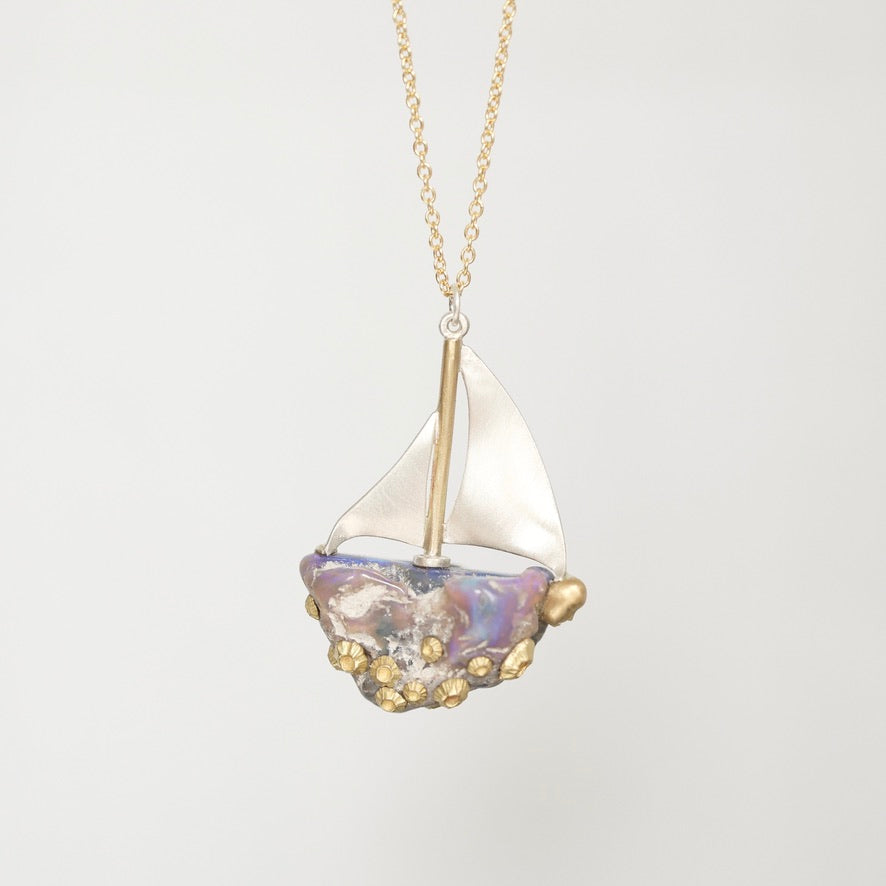 A delicate gold chain necklace featuring a unique sailboat pendant. The sailboat has a white fabric sail, a gold mast, and a hull made from iridescent mother-of-pearl with small gold seed beads along the bottom edge, set against a clean white background.