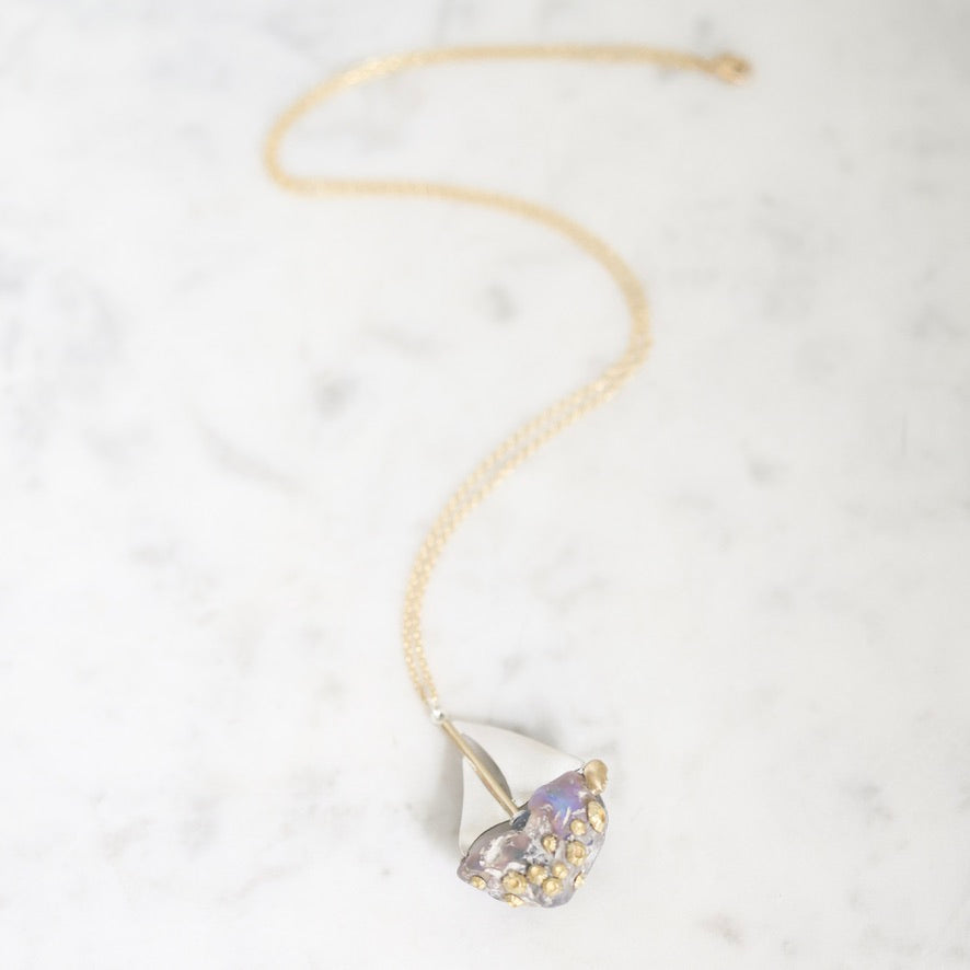A delicate gold chain necklace with a unique teardrop-shaped pendant featuring a light purple crystal and small gold pavé accents, displayed on a white marble surface.
