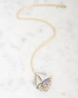 A delicate gold chain necklace with a unique teardrop-shaped pendant featuring a light purple crystal and small gold pavé accents, displayed on a white marble surface.