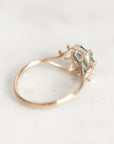 A close-up shot of a vintage-style ring featuring a gold-toned band and a bezel-set teal gemstone, resting on a light marble surface.